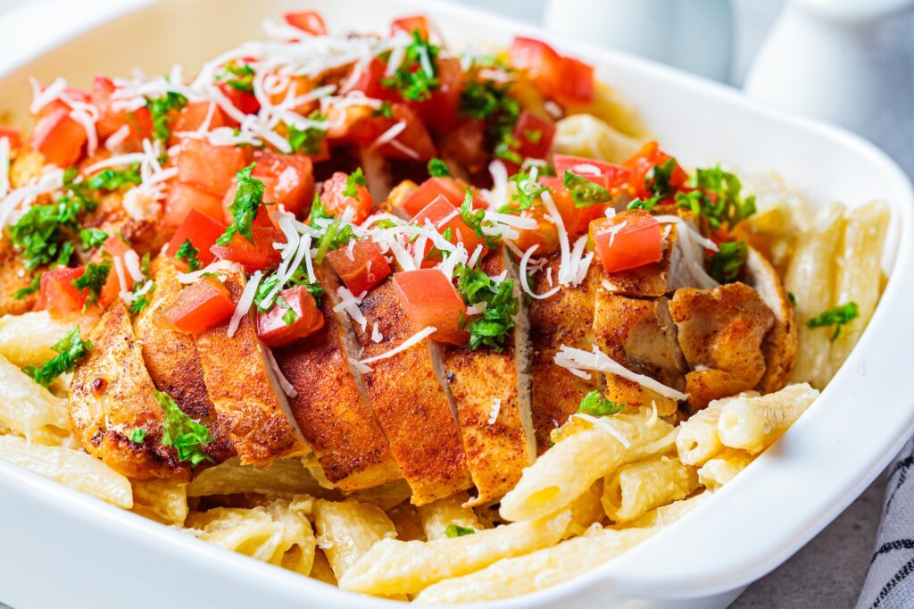Cajun chicken pasta with cheese and tomato in white dish.