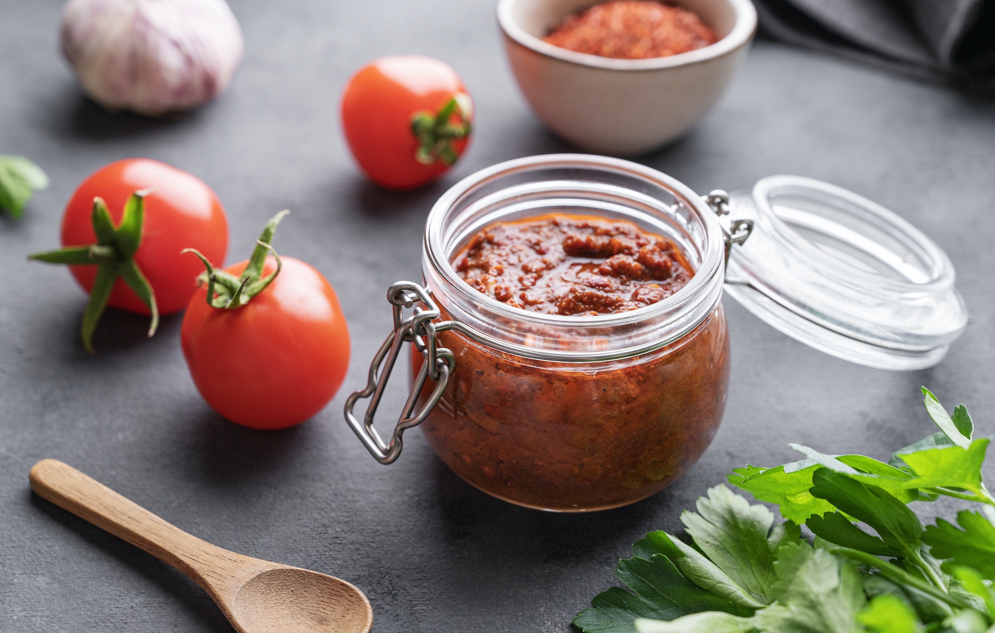 Homemade tomato sauce for pizza or pasta in a jar on a dark background with fresh vegetables