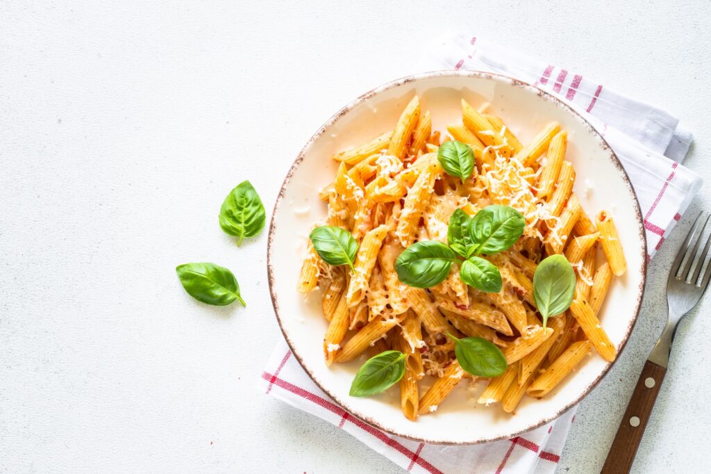 Italian pasta with tomato sauce, basil and parmesan cheese on white table.