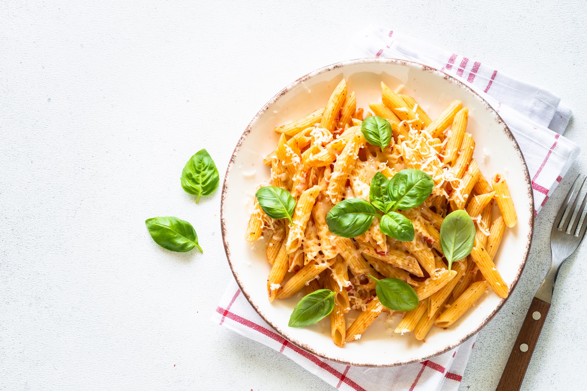 Italian pasta with tomato sauce, basil and parmesan cheese on white table.