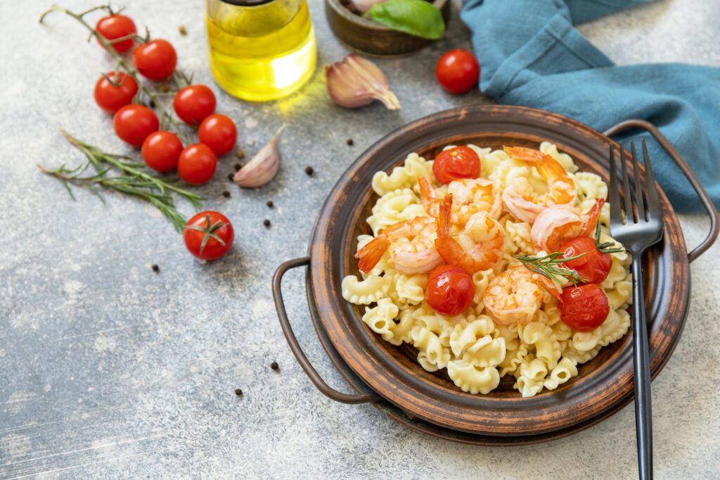 Mediterranean cuisine, seafood diet. Italian creste di gallo pasta with grilled prawns and tomatoes.