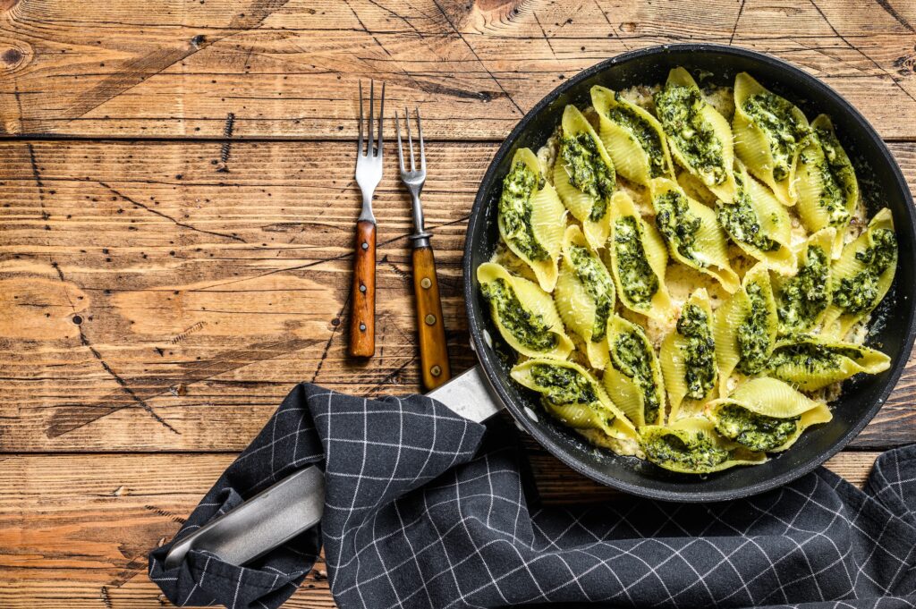 Pasta shells Conchiglioni stuffed with spinach and cheese baked with sauce in a pan.