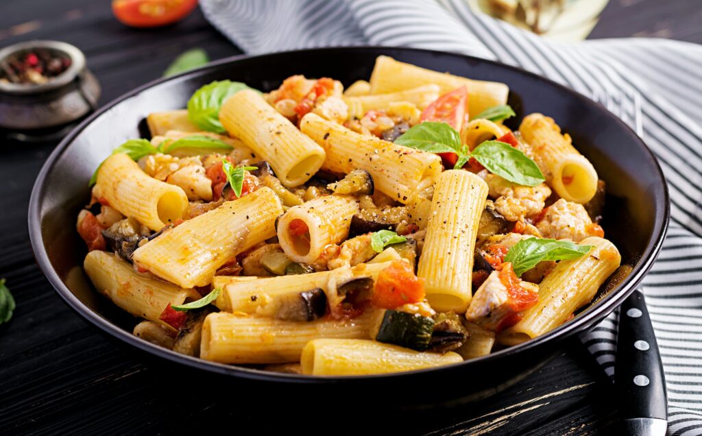 Rigatoni pasta with chicken meat, eggplant in tomato sauce in bowl. Italian cuisine.