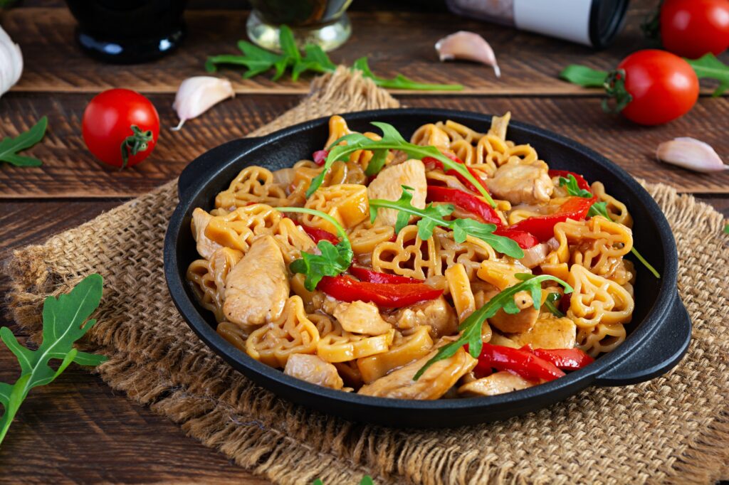 Tasty pasta in tomato sauce with chicken, pepper and herbs on wooden background